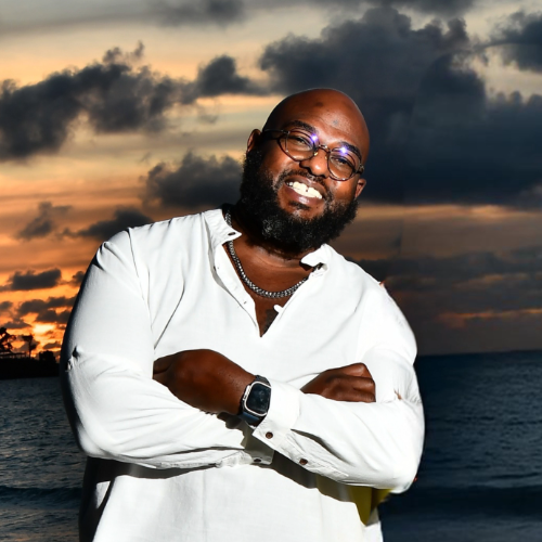 Dr. Corey J. Henderson smiling with arms crossed near the ocean at sunset